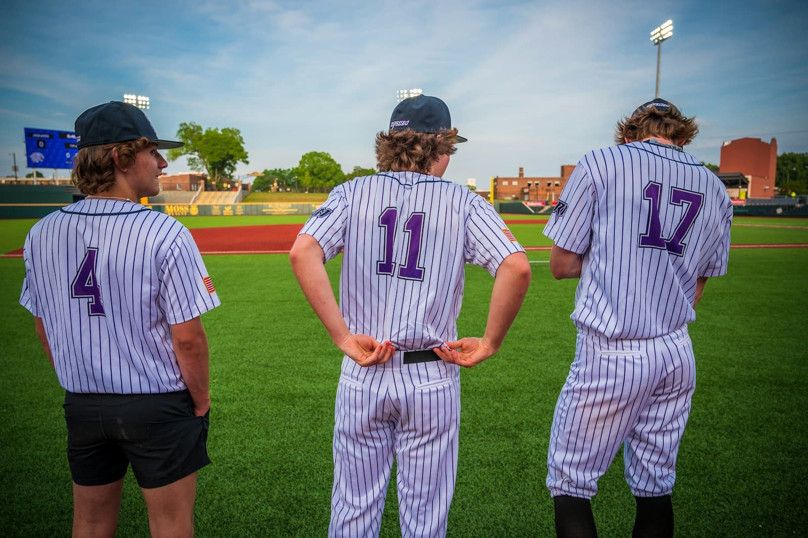 Three young players in pinstripes seen from behind, waiting in the outfield.